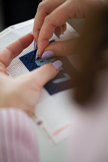close up of hands stitching a navy blue hand painted needlepoint design by Rachel Barri